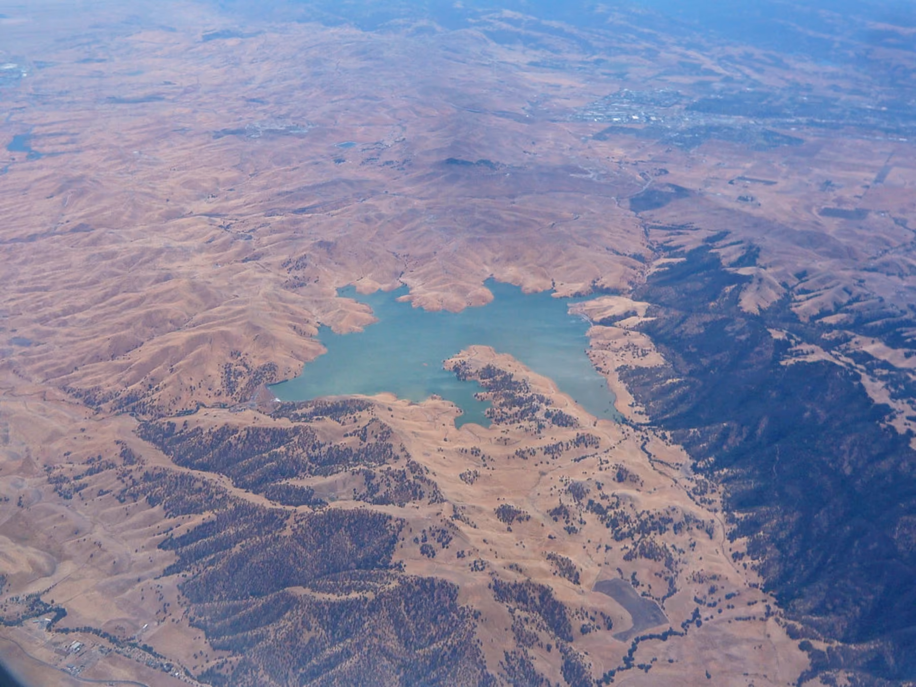 An aerial view of Los Vaqueros Reservoir, blue water held in dry brown hills.