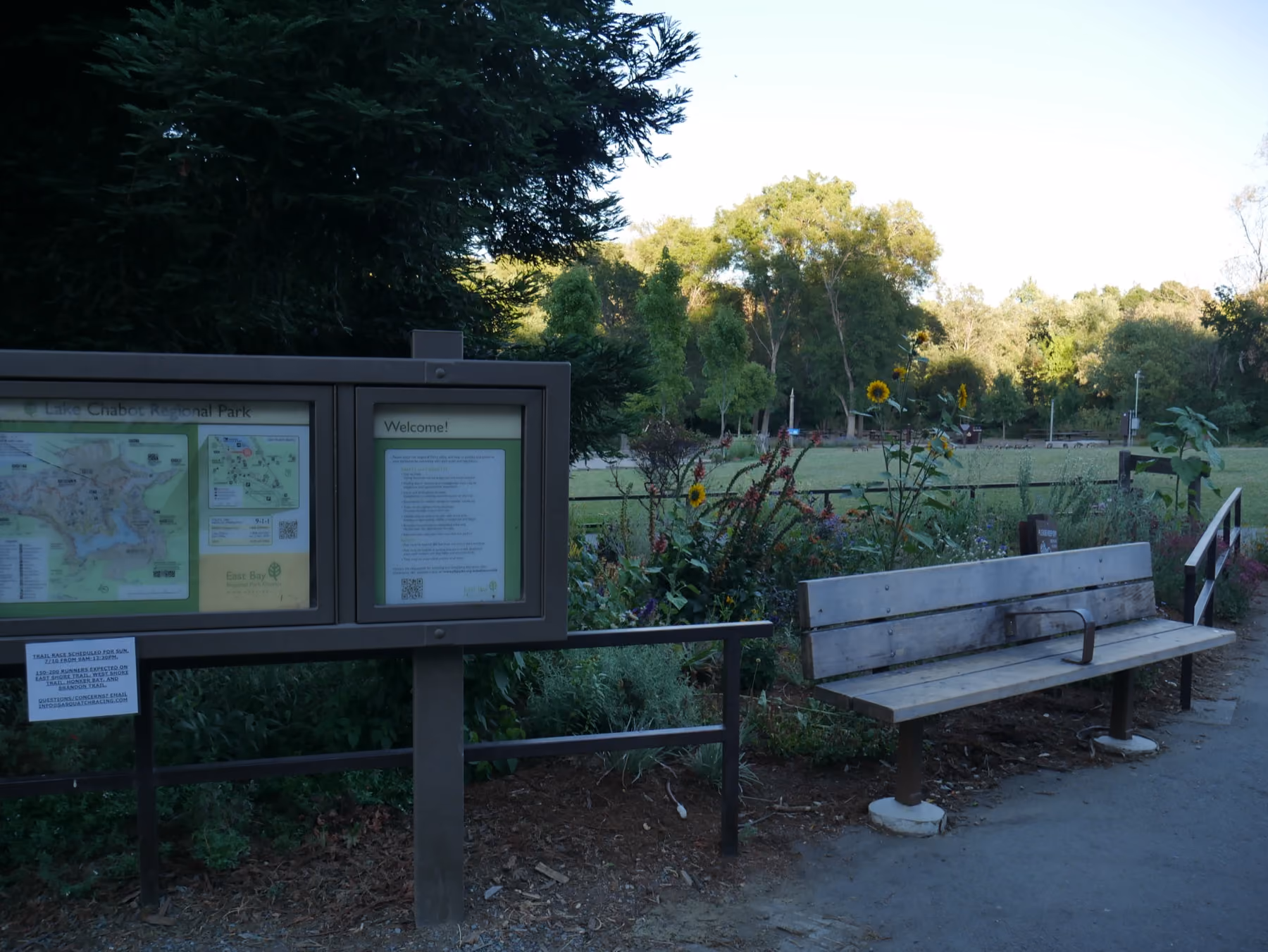 A bench and a trail map board under trees at Lake Chabot Regional Park.