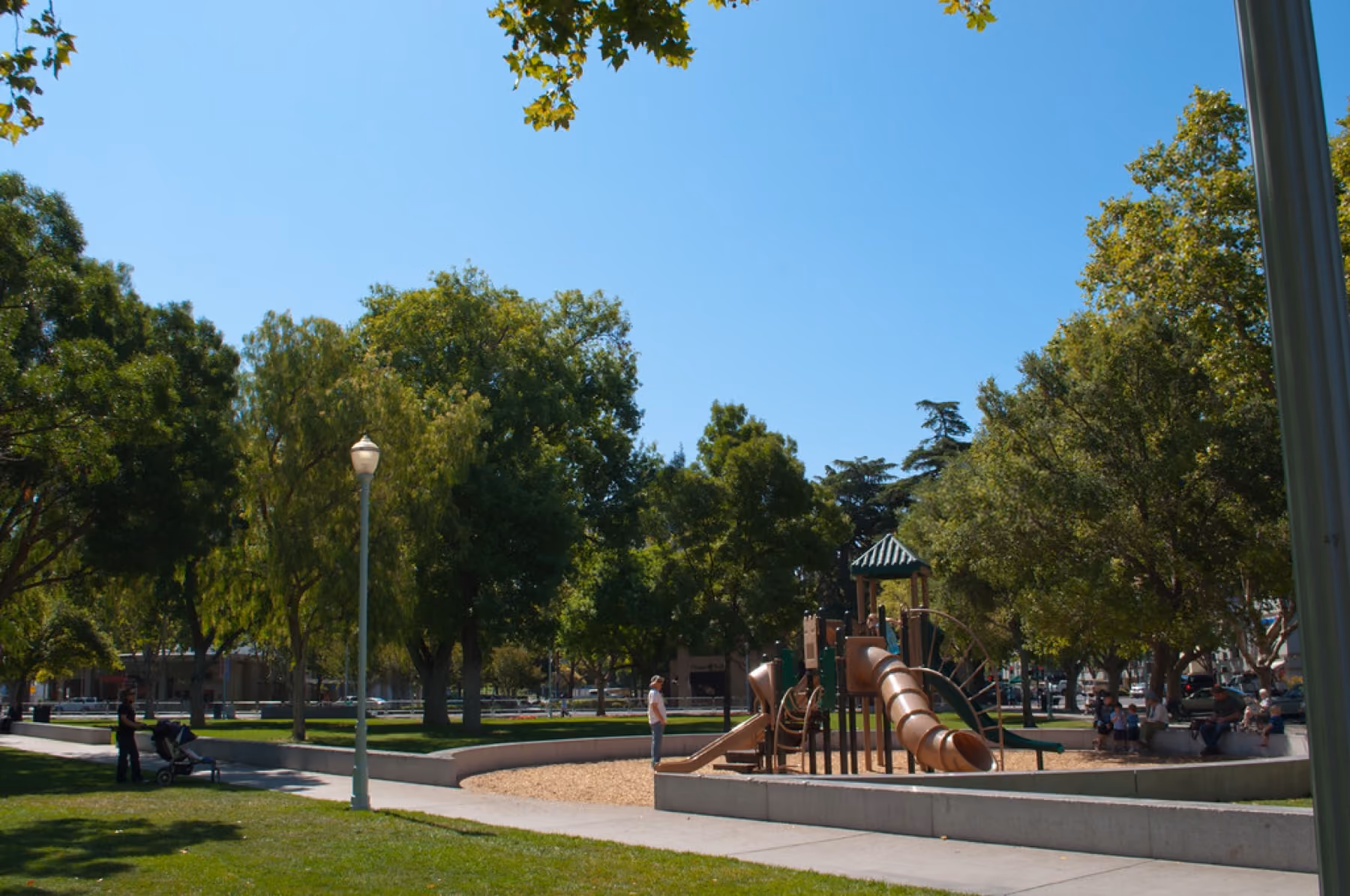 Trees, lawn and a playground in Todos Santos Plaza on a summer day.