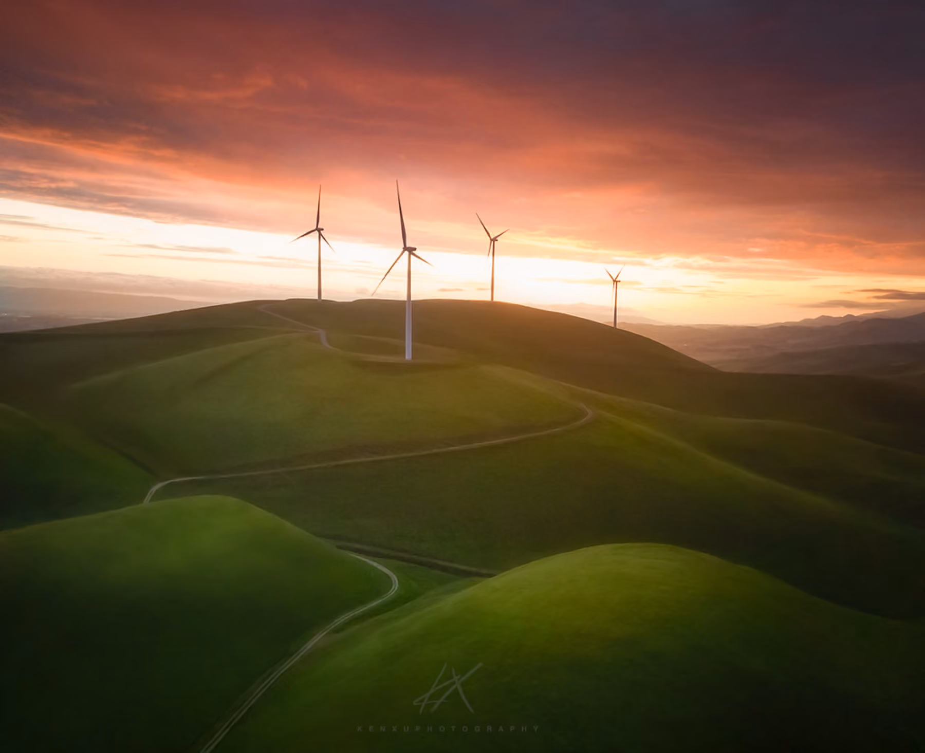 Green grass hills with wind turbines on the ridge at sunset.