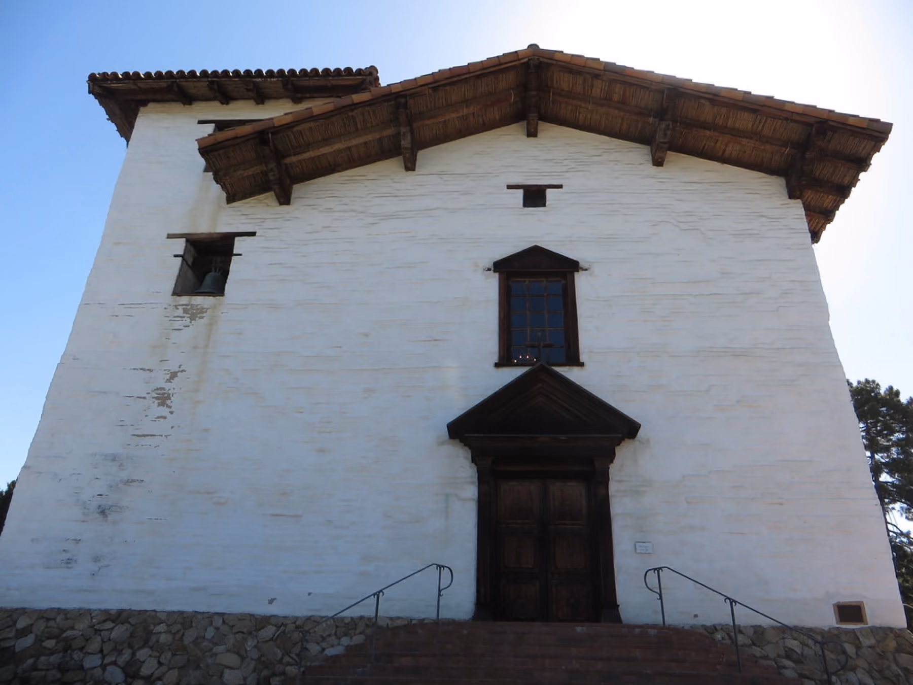 The white adobe front of Mission San José with its wooden door and bell.