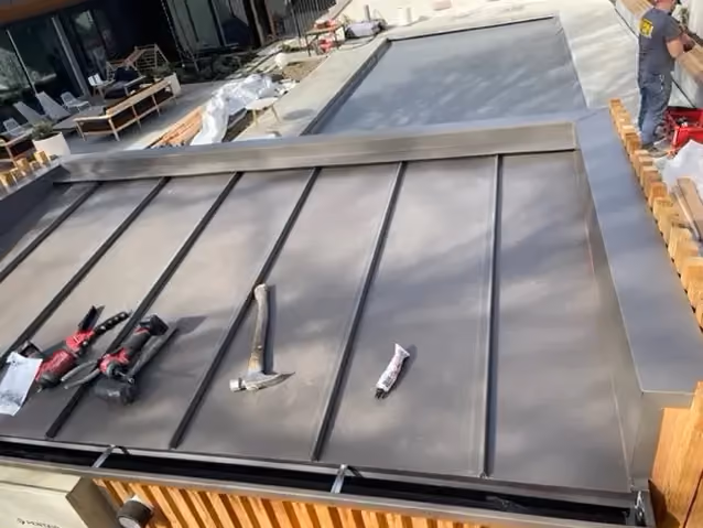 Standing-seam metal panels part way down a low-slope roof, with tools resting on the finished pan.