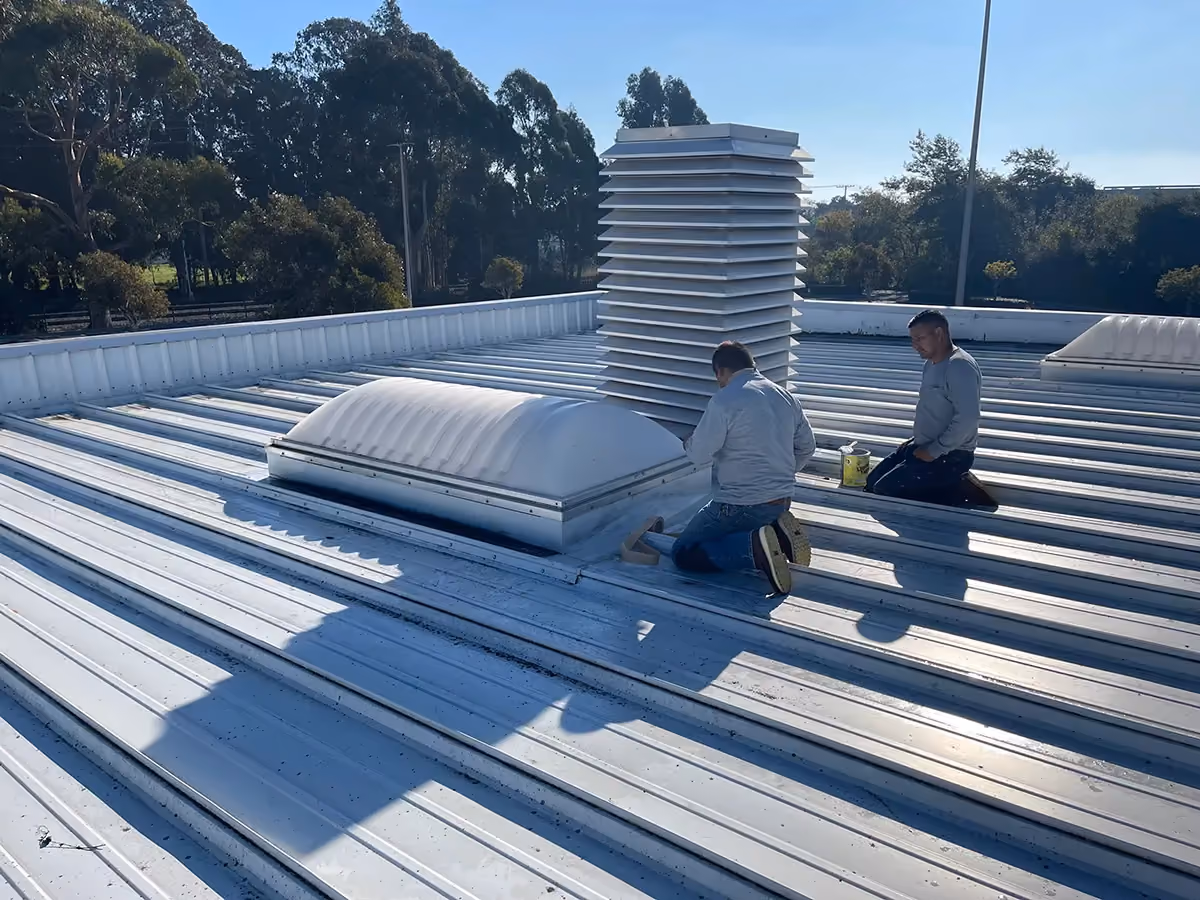 Two of the crew sealing a domed skylight into a white metal roof.