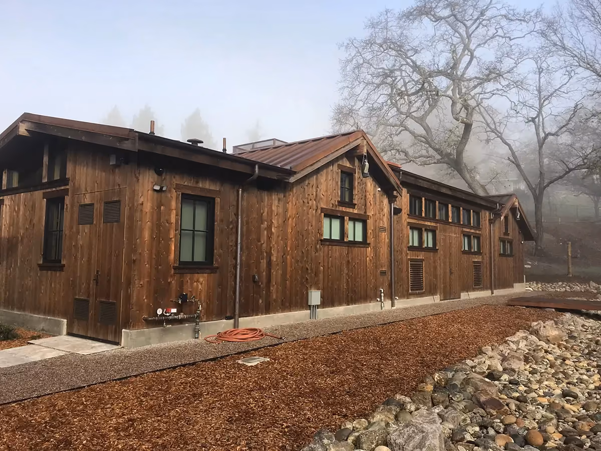 A long wood-clad building under a standing-seam metal roof, downspouts carried down to the corners.
