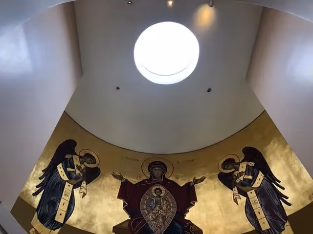 A circular skylight seen from the room below, daylight falling on a gilded mural beneath it.