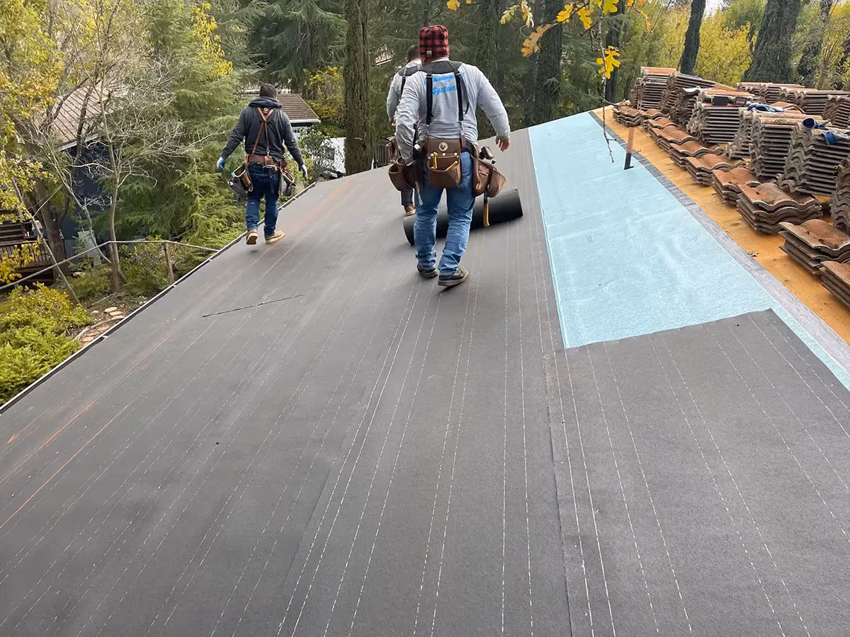 A roofer walking a deck part way through a re-roof, underlayment laid and the old tile stacked to one side.