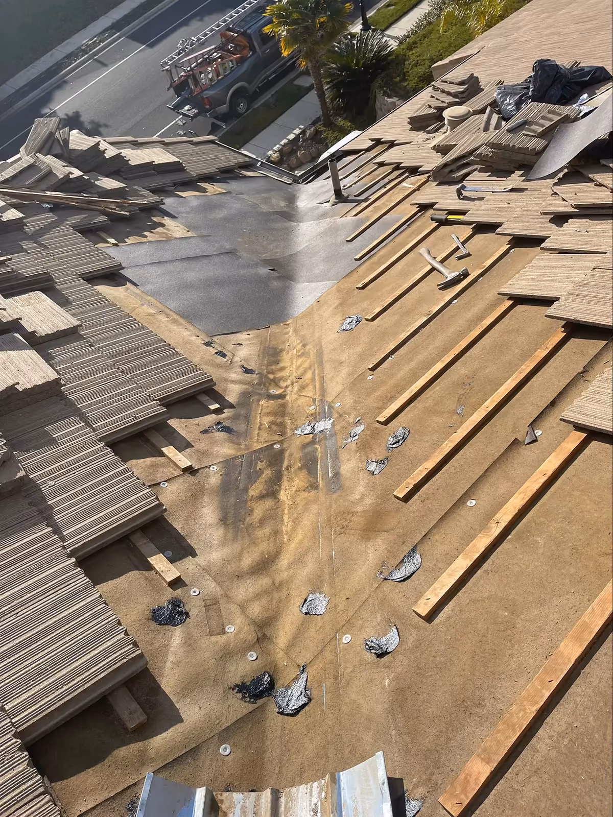 A tile roof mid-replacement seen from above, tiles stacked on the battens and new underlayment beneath.