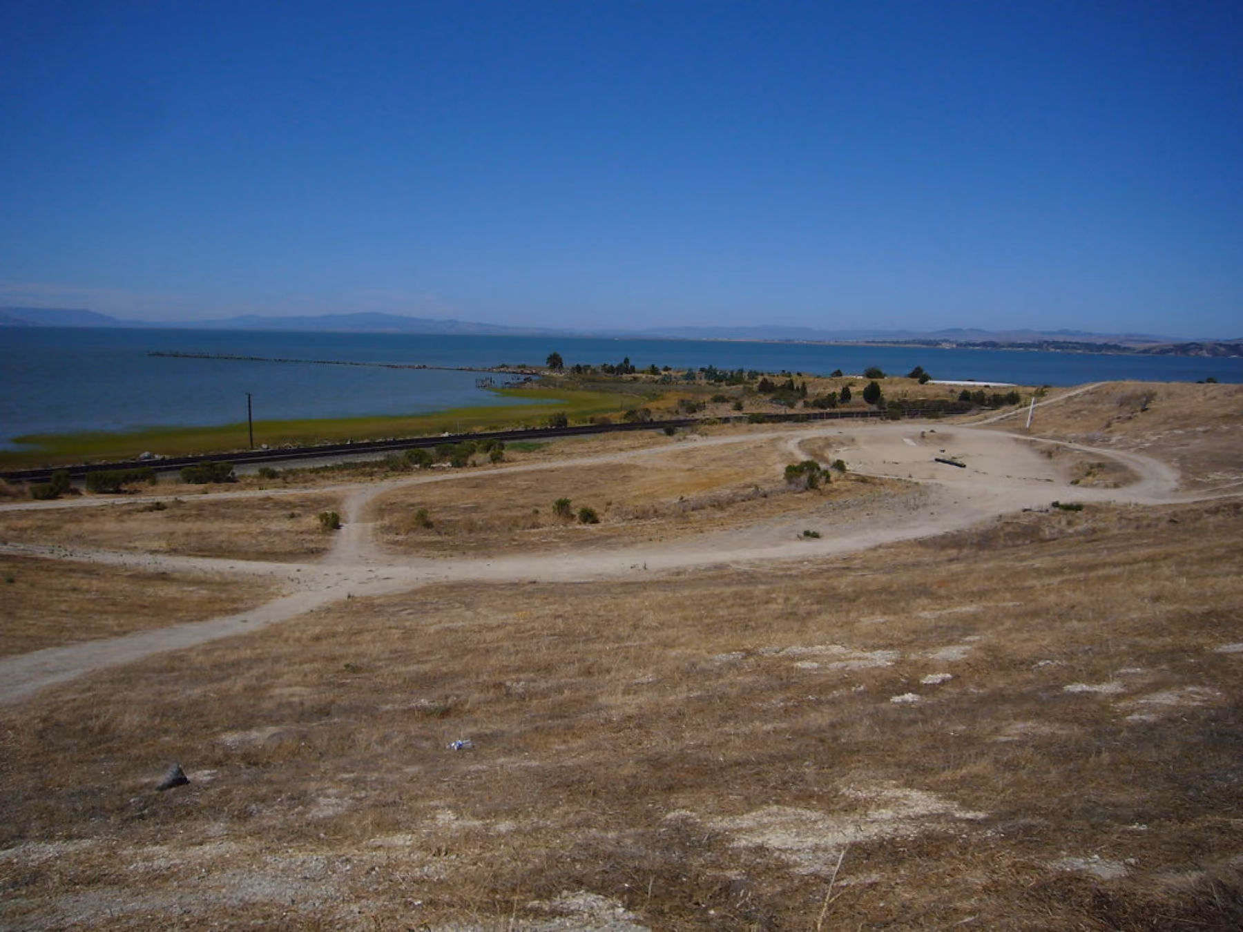 A gravel path along the old quarry shoreline at Hercules, the bay flat beyond.