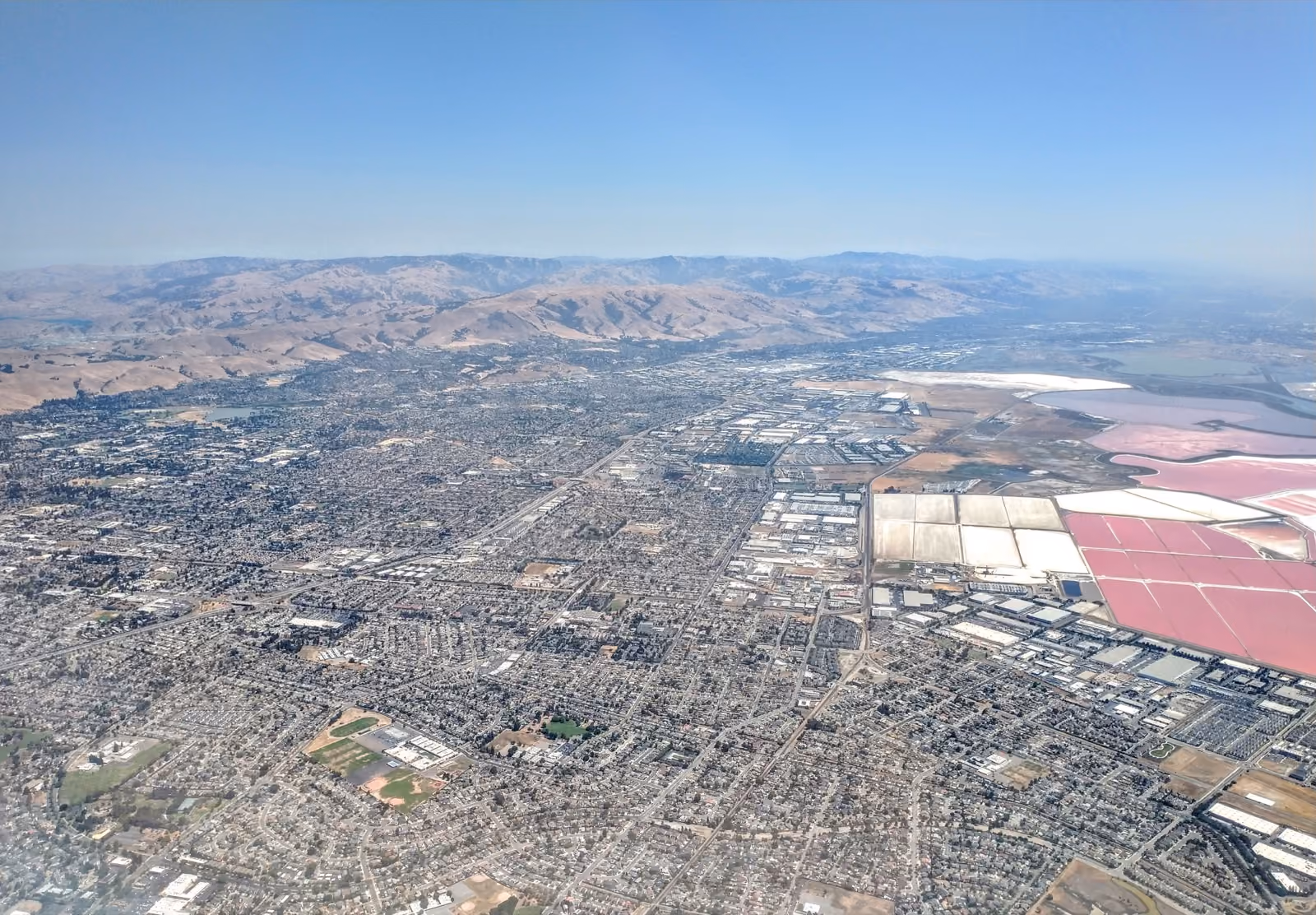 Flat streets and rooftops from the air, salt ponds and hills beyond them.