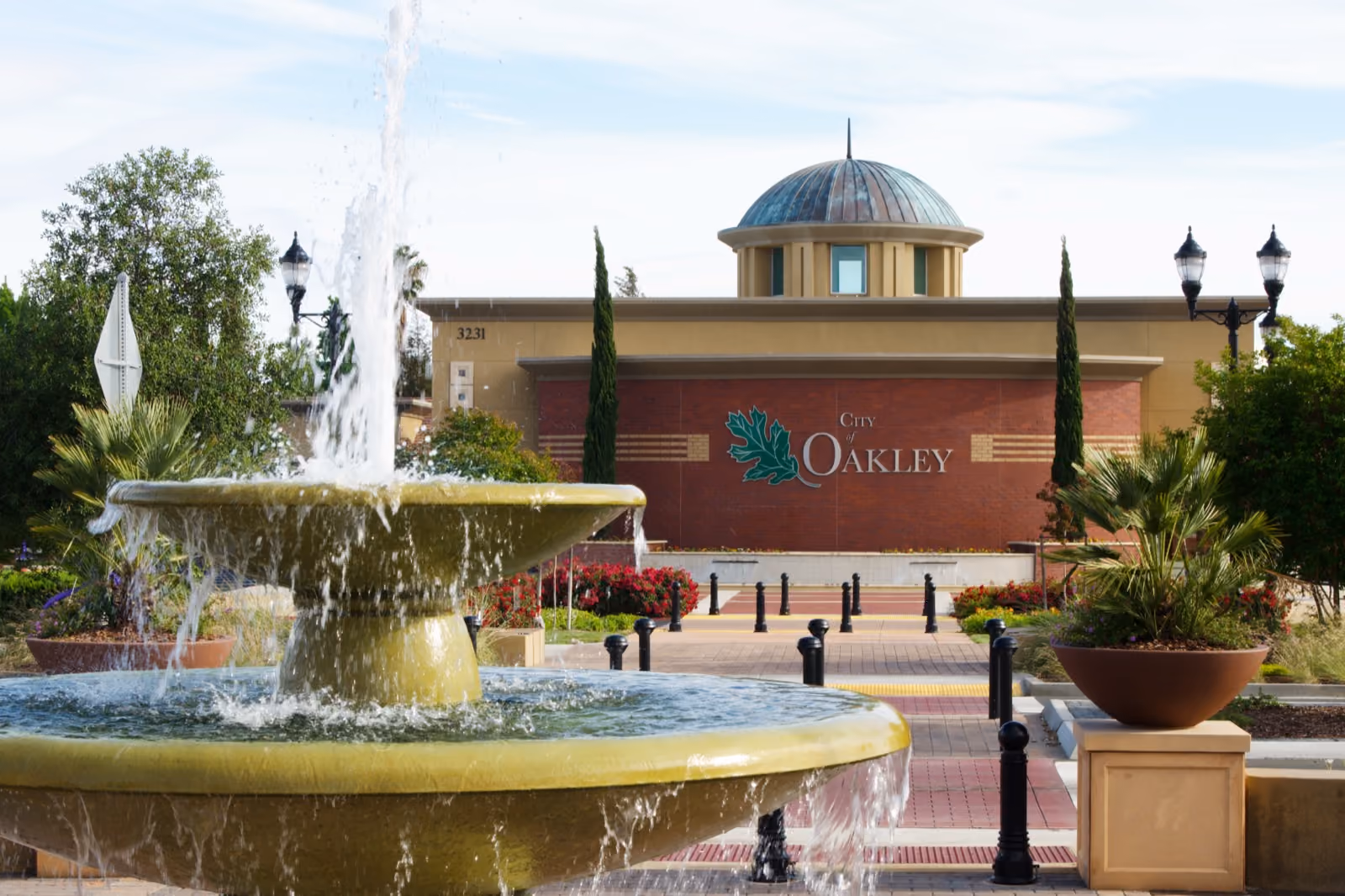 A tiered fountain playing in front of a brick civic building with a domed cupola.