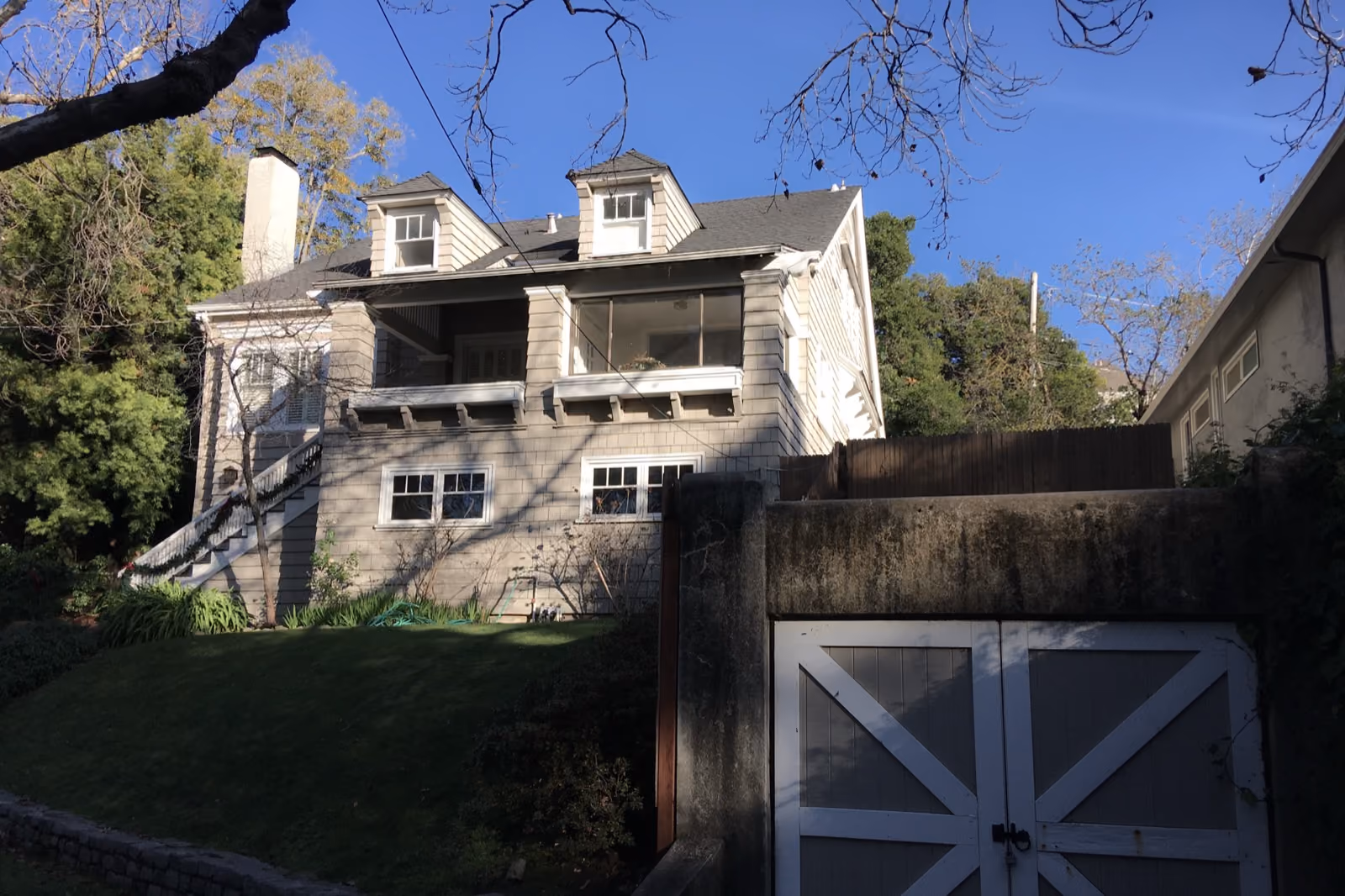 A shingled house standing above a garage cut into the slope beneath it.