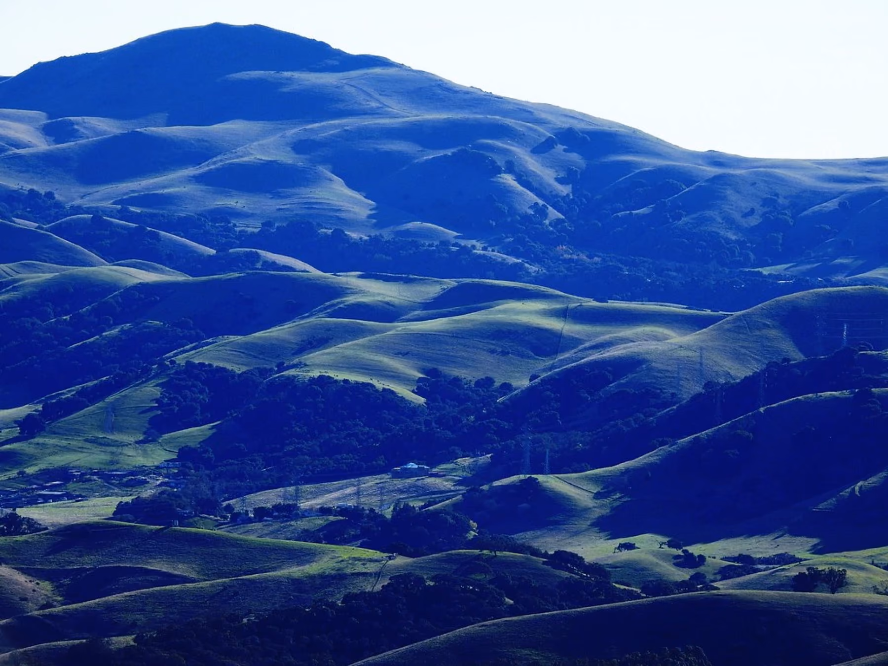 Green ridges folding into one another above Pleasanton under a blue haze.