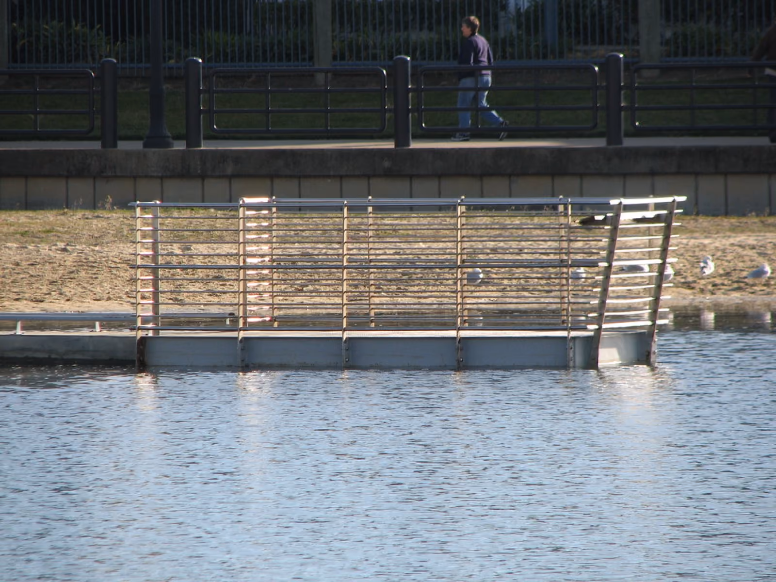 A long steel and timber memorial frame standing in shallow water at high tide.