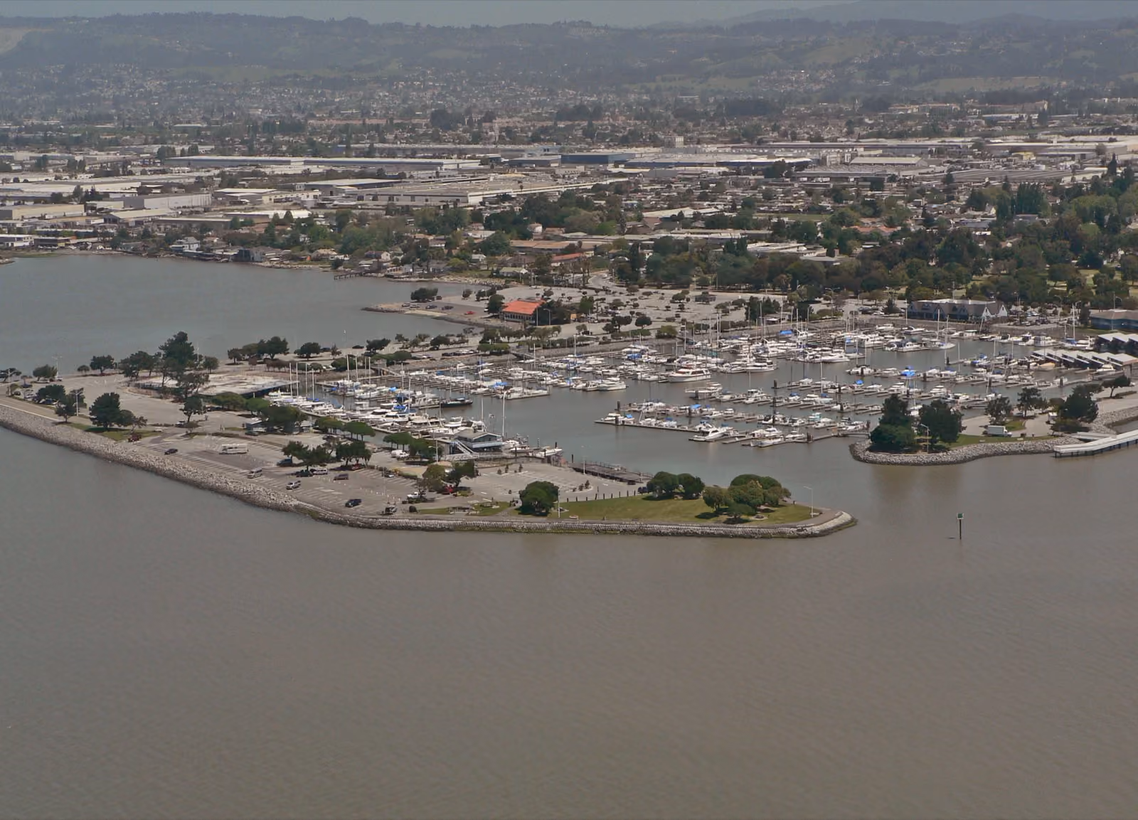 Moored boats filling a marina basin, the bay and the flat shore beyond.