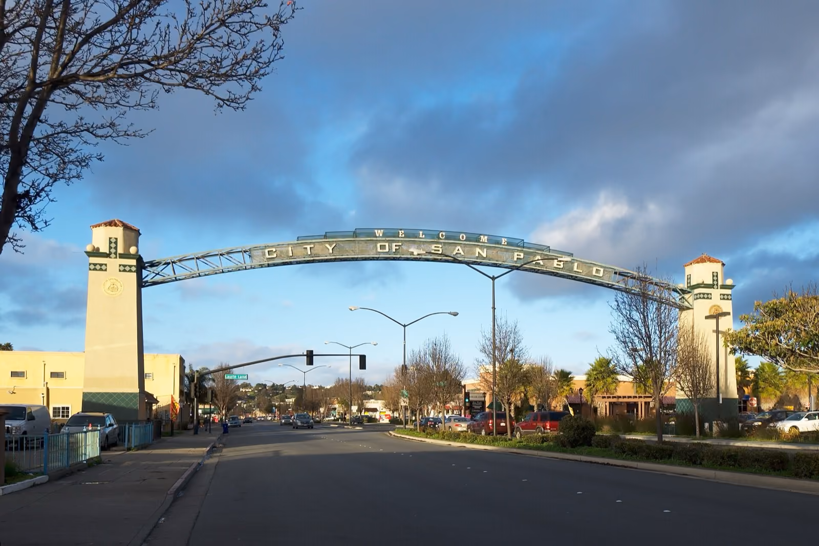 A green arch spanning a wide road between two towers, under a dark evening sky.